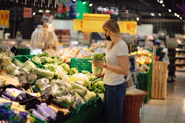 Beautiful young woman mask chooses vegetables herbs supermarket proper nutrition everyday lifestyle natural food products personal protective equipment social life epidemic